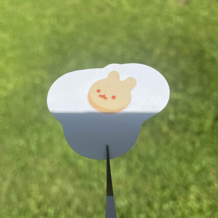 A peeled off kiss cut sticker being held with tweezers outside in front of grass showing a sunny side up egg with a bunny face and ears on it.